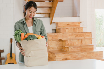 Asian women holding grocery shopping paper bags at home, young Asia girl happy buy vegetables and fruit healthy and organic product  from supermarket put it in kitchen in the morning concept.