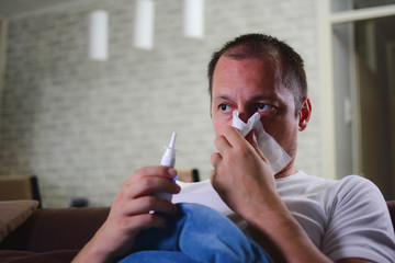 Wall Mural - Sick man with paper napkin blowing nose. Ill man blowing his nose and sitting on the bed covered with warm blanket. Rhinitis concept.