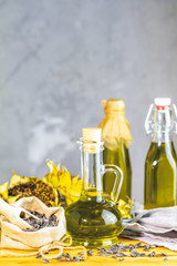 Various types of oil in bottles, dried sunflowers and seeds on wooden table.