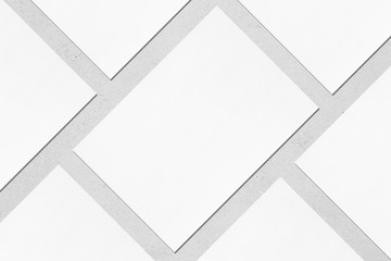 Close up of empty white rectangle poster mockups lying diagonally with soft shadow on neutral light grey concrete background. Flat lay, top view. Open composition.