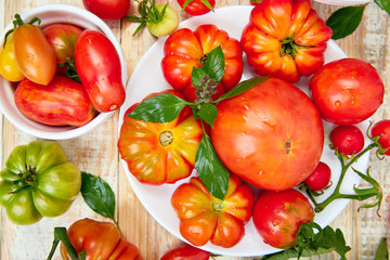 Mix of tomatoes background. Beautiful juicy organic red tomatoes on white wooden table background. Clean eating concept. Copy space, flat lay..