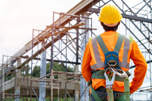 Construction worker wearing safety harness and safety line working at high place,Practices of occupational safety and health can use hazard controls and interventions to mitigate workplace hazards.