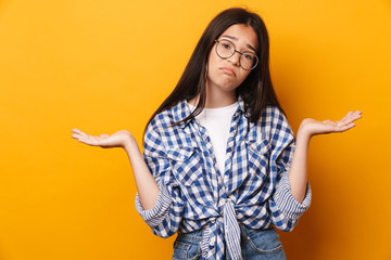 Canvas Print - Confused unsured young cute teenage girl in glasses posing isolated over yellow wall background.