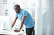 © AnnaStills - African young designer in eyeglasses and casual wear standing near the table and looking at computer monitor at office