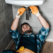 © LIGHTFIELD STUDIOS - bearded repairman fixing water damage with adjustable wrench in bathroom
