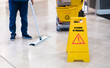 Janitor Cleaning Floor In Front Of Yellow Caution 