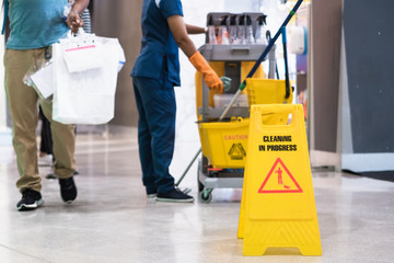 Janitor Cleaning Floor In Front Of Yellow Caution 