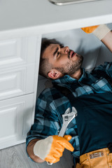 Wall Mural - selective focus of handsome repairman holding adjustable wrench while working in kitchen