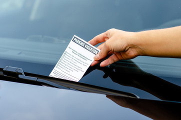 Close-up Of A Woman Taking Parking Ticket On Car's Windshield