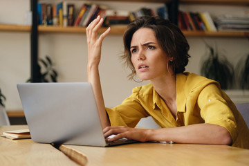 Aufkleber - Young brunette woman indignantly sitting at table and working on laptop in office