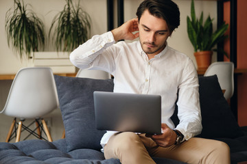 Aufkleber - Young attractive businessman sitting on sofa dreamily working on laptop in co-working space