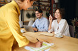 © Anton - Group of cheerful business colleagues sitting at the desk with laptop and papers while happily talking at work in modern office
