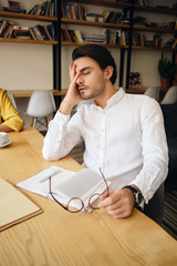 Aufkleber - Young tired man sitting at the table with notepad leaning head on hand sleeping at work in modern office