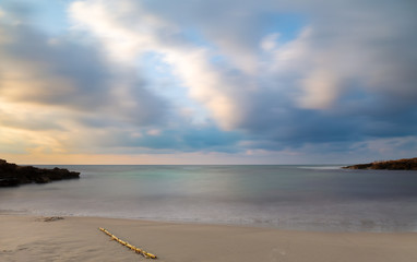 Wall Mural - Soft waves through long exposure. A beautiful bay with a sandy beach in the early morning before sunrise near the Spanish town of Torrevieja. Colorful clouds in the sky.