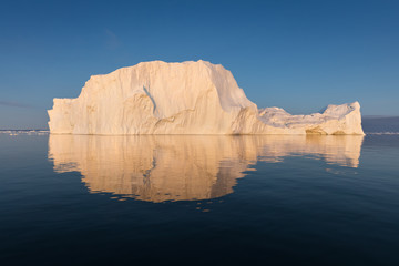 Wall Mural - Photogenic and intricate iceberg under an interesting and blue sky during sunset. Effect of global warming in nature. Conceptual image of melting glacier in deep blue water in Antarctica or Greenland