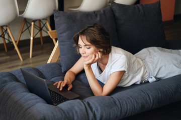 Aufkleber - Young beautiful woman lying on sofa dreamily working on laptop in co-working space