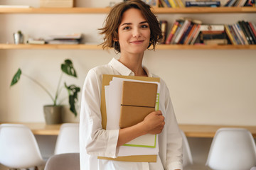 Aufkleber - Young beautiful smiling woman dreamily looking in camera with papers and notepad in office
