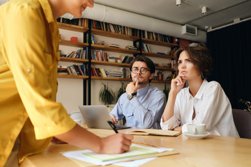 Aufkleber - Young serious business colleagues sitting at the desk with laptop thoughtfully looking at boss while discussing new project together in modern office