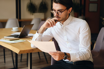 Aufkleber - Young serious businessman in eyeglasses thoughtfully reading papers while working in modern office