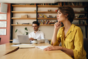 Aufkleber - Side view of young woman sitting at the table with notepad thoughtfully working with colleague on background in office