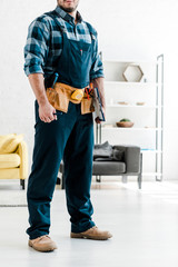 Wall Mural - cropped view of bearded worker in safety helmet holding clipboard in living room