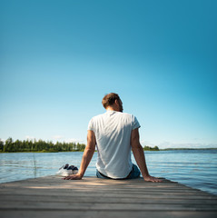 Wall Mural - Mann sitzt im Sommer in Finnland auf einem Holzsteg am See