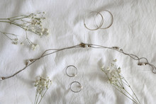 Silver And Gold Jewelry And Gypsophila Flowers On White Sheets. Top View.