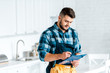 © LIGHTFIELD STUDIOS - handsome bearded workman writing while holding clipboard in kitchen