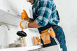 © LIGHTFIELD STUDIOS - cropped view of handyman with tool belt holding plunger in kitchen
