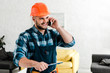 © LIGHTFIELD STUDIOS - cheerful worker in safety helmet holding clipboard while talking on smartphone