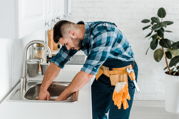 Wall Mural - handsome bearded repairman working near sink in kitchen