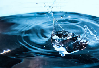 Water splash. Ice cubes falling into the blue water. Splash of ice water. Water splashes from falling ice cubes