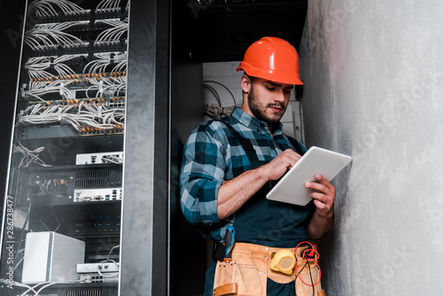 Fotomural handsome bearded technician in safety helmet holding digital tablet
