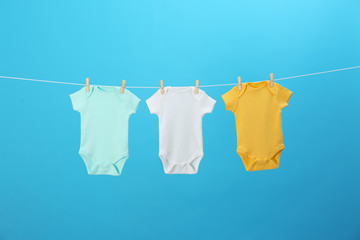 Colorful baby onesies hanging on clothes line against blue background. Laundry day