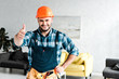 © LIGHTFIELD STUDIOS - cheerful worker in safety helmet looking at camera while showing thumb up
