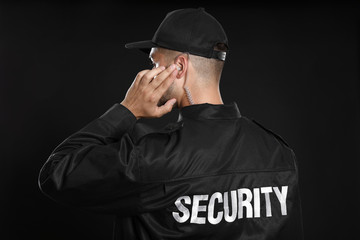 Wall Mural - Male security guard in uniform using radio earpiece on dark background