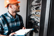 © LIGHTFIELD STUDIOS - technician in safety helmet holding clipboard while looking at wires and cables