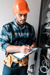 © LIGHTFIELD STUDIOS - handsome technician holding clipboard while writing near wires and cables