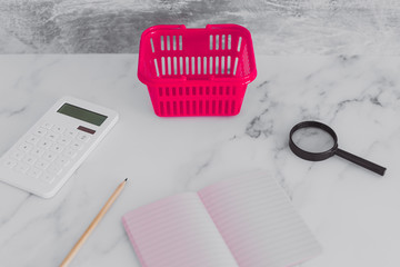 pink shopping basket on marble desk with shopping list notebook magnifying glass and calculator