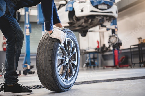 Cuadros en Lienzo Male mechanic hold and rolling tire at repairing service garage background