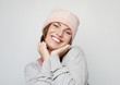 © Raisa Kanareva - Funny young woman in a pink beanie hat makes faces and poses over light grey background