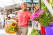 © Dragana Gordic - Portrait of a beautiful senior woman doing shopping in a market on a sunny morning, she carries a basket with fruits and vegetables and a bouquet of flowers. Woman buying flowers on the local market..