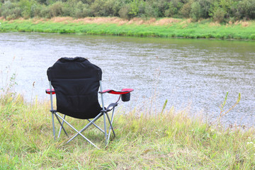 Portable folding tourist red armchair on green grass in summer on picnic near river