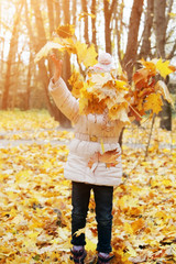 happy girl throws yellow maple leaves in sunny park. kid enjoy autumn weather outdoors