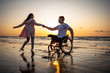 © Nejron Photo - Handicapped man in wheelchair and his girlfriend on a beach at sunset