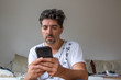 © Michael Eichhammer - Mann mit Handy daheim  tippt schlechtgelaunt