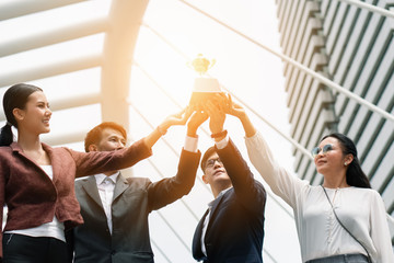 asian business people holding and raise first place trophy together showing team spirit to win business competition awards