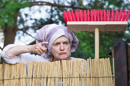 Fotografía An aggressive, elderly woman with a headscarf and broom scolds at the garden fence