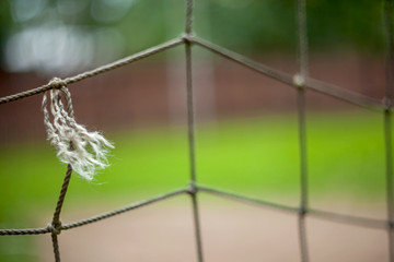 A torn old rope net from a football goal with a dry thread end and knots and a blurred background.