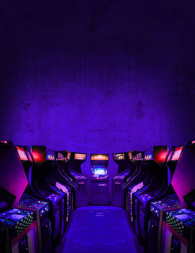 Old Unbranded Vintage Arcade Video Games in dark gaming room with purple light with glowing displays and concrete wall - vertical photo of retro design with free copy space for a poster or magazine